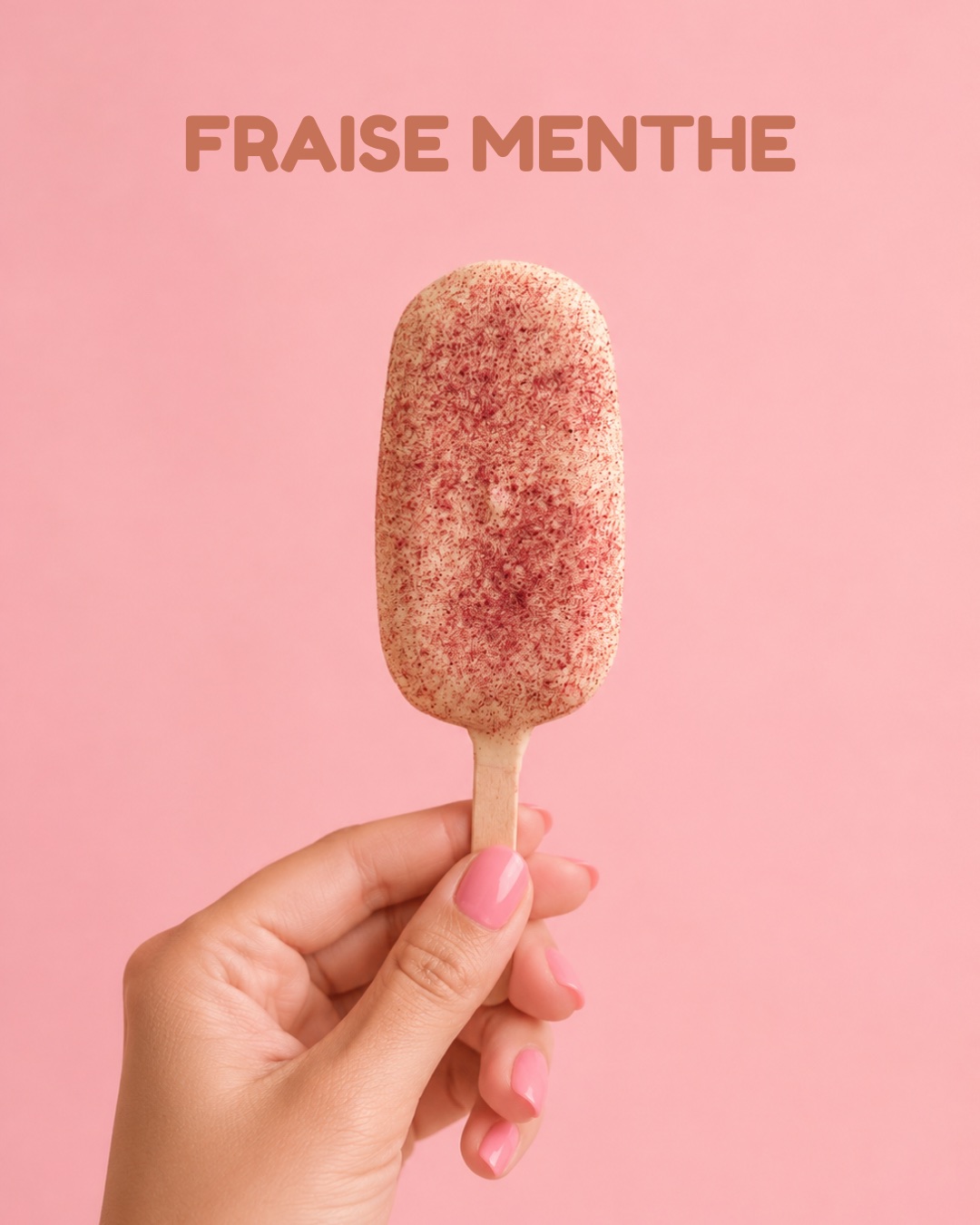 Bâtonnet glacé Fraise Menthe tenu à la main, sur fond rose
